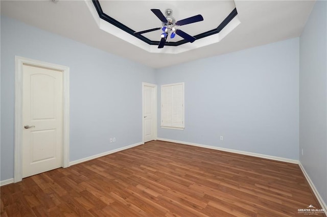 empty room with baseboards, a ceiling fan, a raised ceiling, and wood finished floors