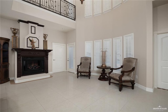 sitting room with tile patterned flooring, a glass covered fireplace, a towering ceiling, and baseboards