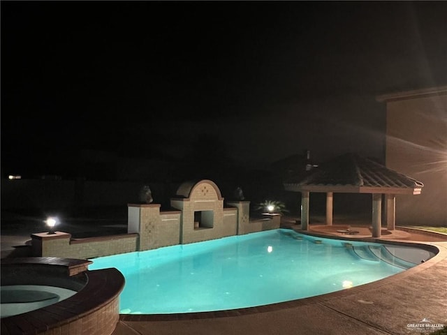 pool at night featuring a pool with connected hot tub, a patio, and a gazebo