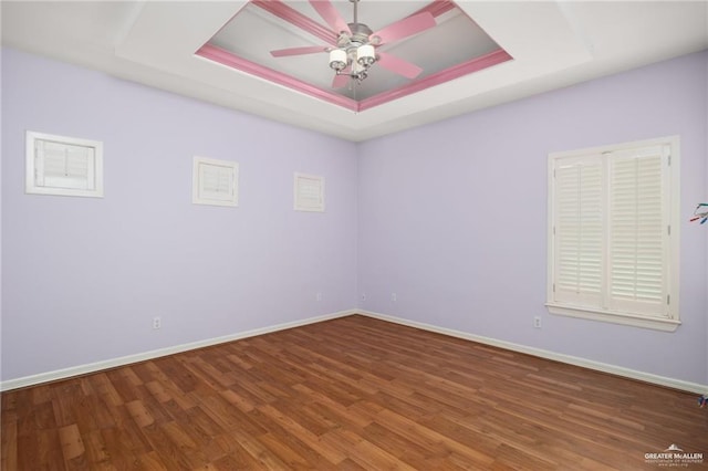 unfurnished room featuring wood finished floors, a raised ceiling, a ceiling fan, and baseboards