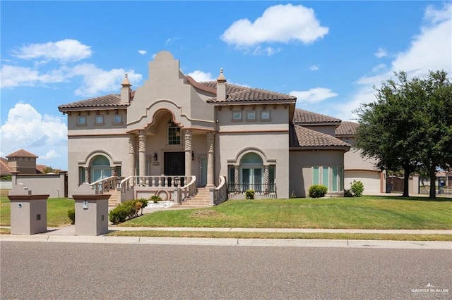 mediterranean / spanish-style home with an attached garage, a tile roof, a front lawn, and stucco siding