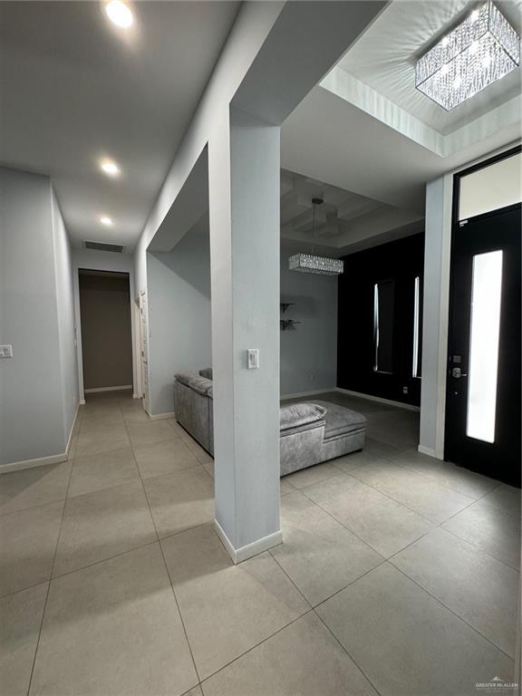 corridor featuring a chandelier, light tile patterned floors, and a tray ceiling