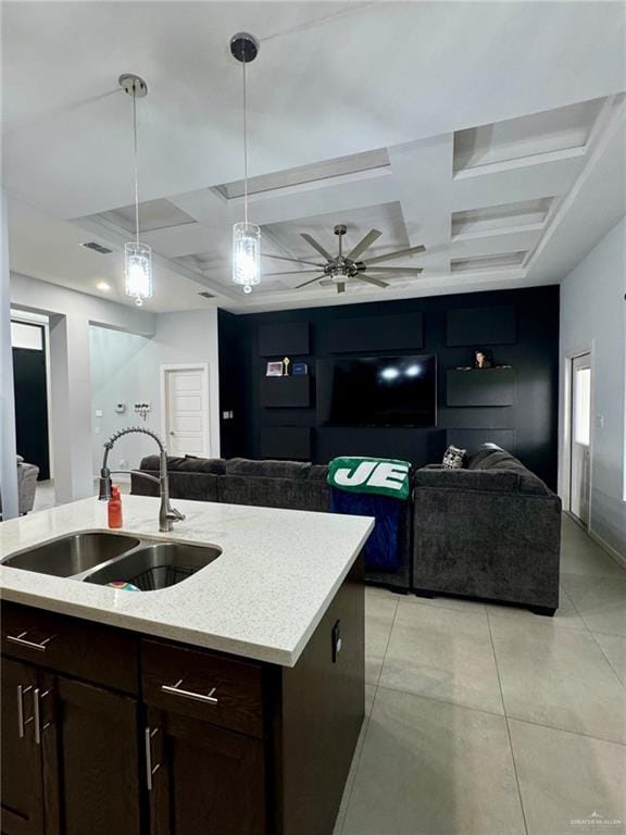 kitchen with coffered ceiling, ceiling fan, sink, decorative light fixtures, and a center island with sink