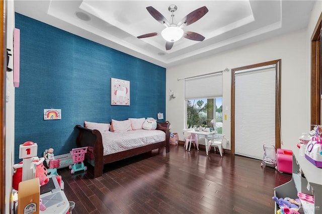 bedroom with ceiling fan, an accent wall, a tray ceiling, and wood finished floors