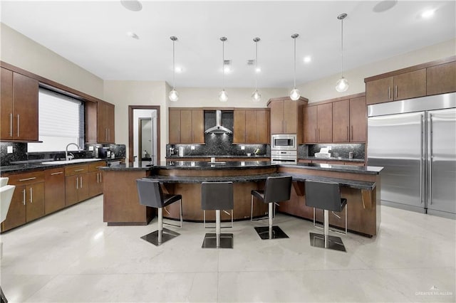 kitchen with built in appliances, wall chimney exhaust hood, a spacious island, and a breakfast bar area