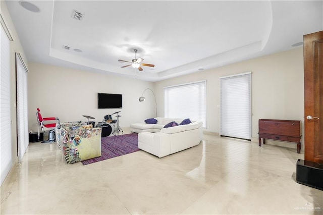 living area with visible vents, a tray ceiling, and a ceiling fan