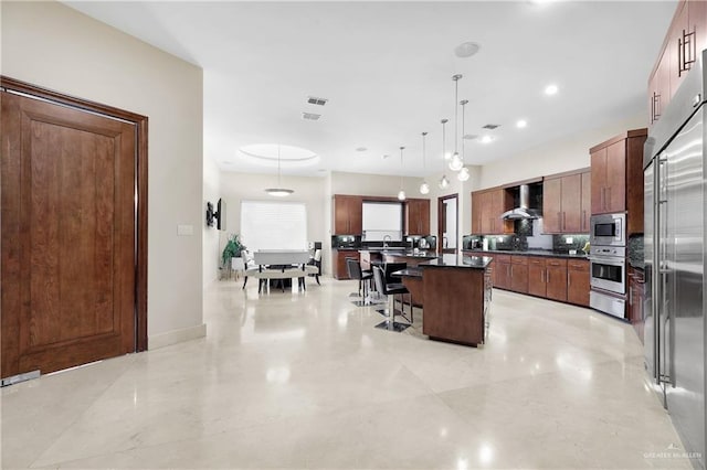 kitchen with dark countertops, wall chimney exhaust hood, appliances with stainless steel finishes, a breakfast bar area, and a warming drawer