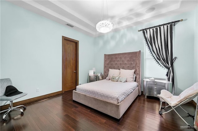 bedroom with a tray ceiling, dark wood-style flooring, visible vents, and baseboards