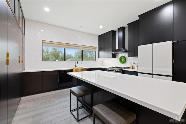 kitchen with wall chimney range hood, black dishwasher, stainless steel range oven, light hardwood / wood-style floors, and a breakfast bar area