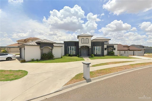 mediterranean / spanish house featuring stucco siding, concrete driveway, a front yard, a standing seam roof, and metal roof