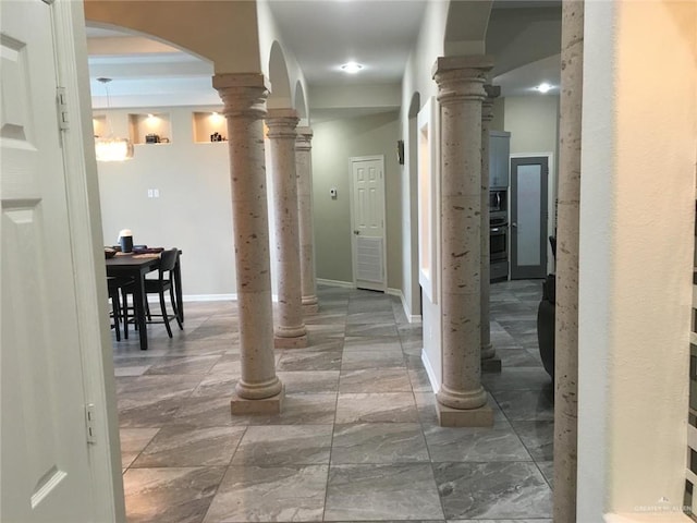 hallway featuring arched walkways, marble finish floor, decorative columns, and baseboards