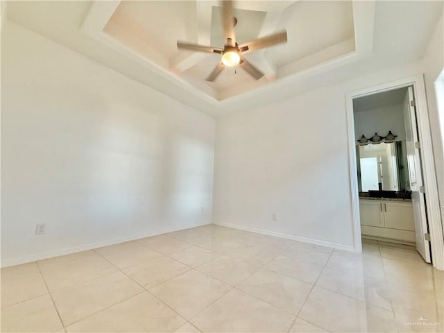 spare room featuring a tray ceiling, light tile patterned flooring, ceiling fan, and baseboards