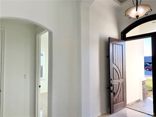 foyer entrance featuring arched walkways, baseboards, and light tile patterned floors