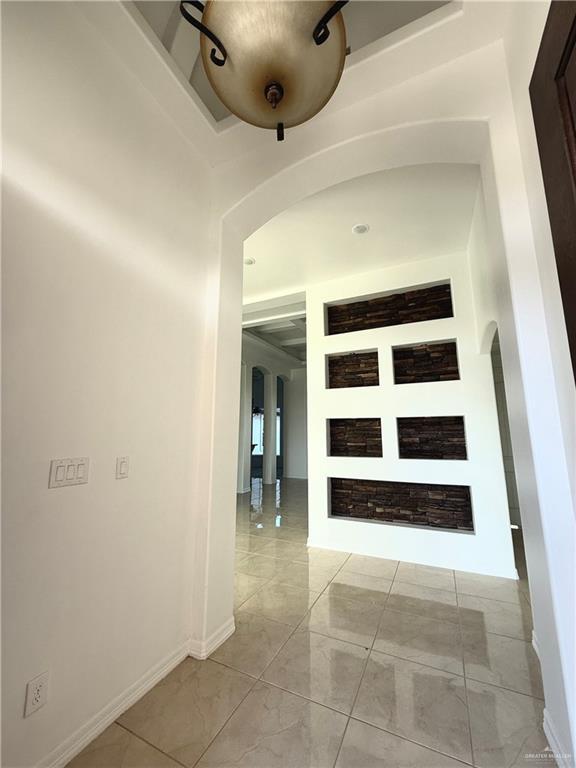 corridor with marble finish floor, baseboards, and arched walkways