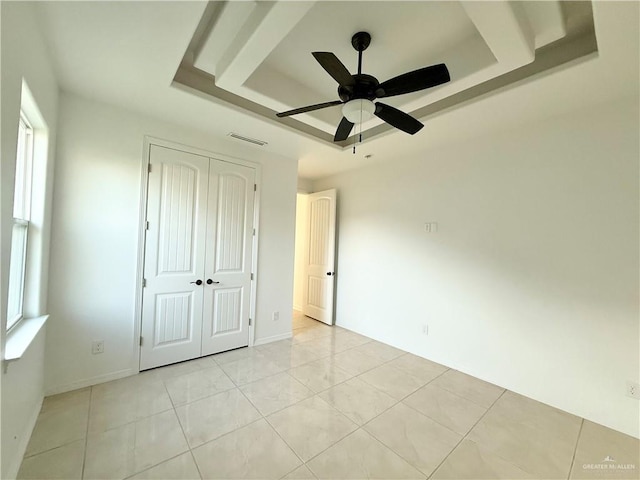 unfurnished bedroom with light tile patterned floors, a closet, a raised ceiling, visible vents, and ceiling fan