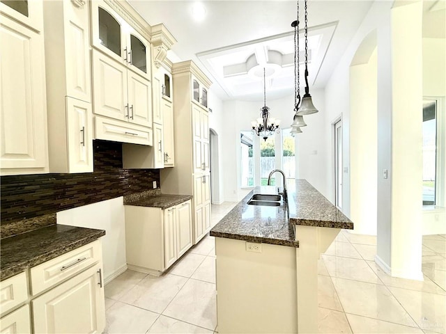 kitchen with a sink, decorative backsplash, dark stone countertops, a center island with sink, and pendant lighting