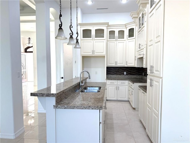 kitchen with tasteful backsplash, white cabinets, a sink, and light tile patterned floors