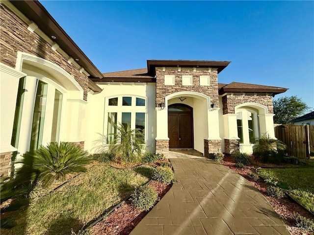 view of exterior entry with stone siding, fence, french doors, and stucco siding