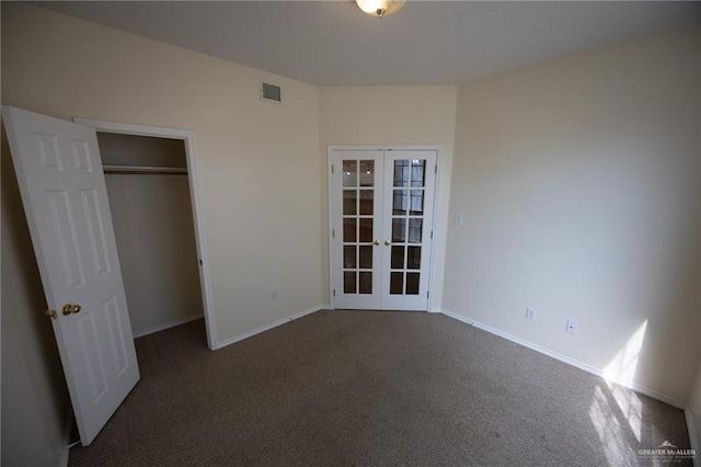 unfurnished bedroom featuring a closet, french doors, and dark carpet