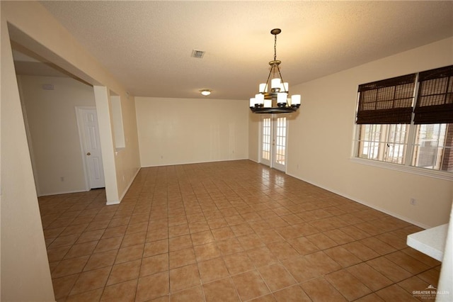 empty room with tile patterned flooring, a textured ceiling, and a notable chandelier