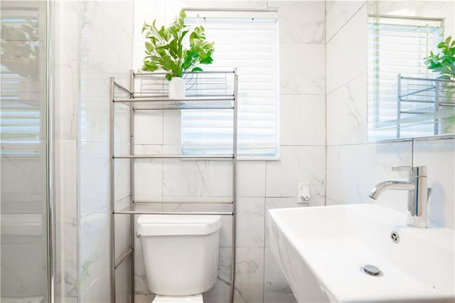 bathroom with tile walls, a sink, toilet, and healthy amount of natural light