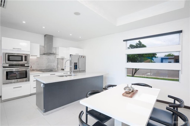 kitchen featuring appliances with stainless steel finishes, wall chimney range hood, a sink, tasteful backsplash, and white cabinets