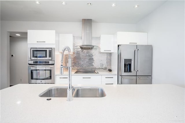 kitchen with appliances with stainless steel finishes, wall chimney range hood, a sink, white cabinetry, and tasteful backsplash