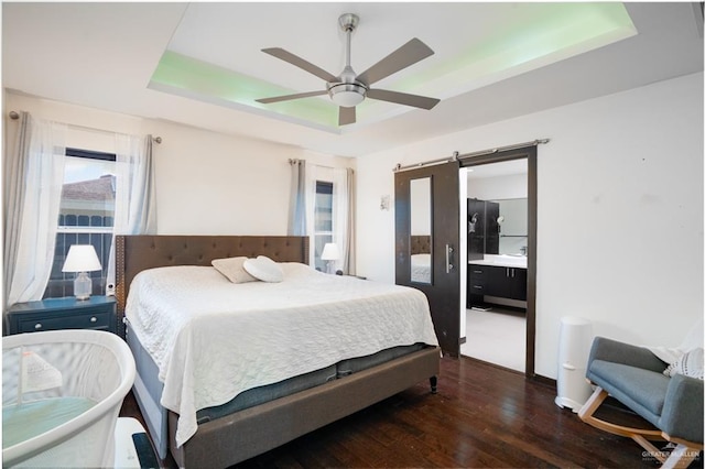 bedroom with a tray ceiling, wood finished floors, a barn door, ceiling fan, and baseboards