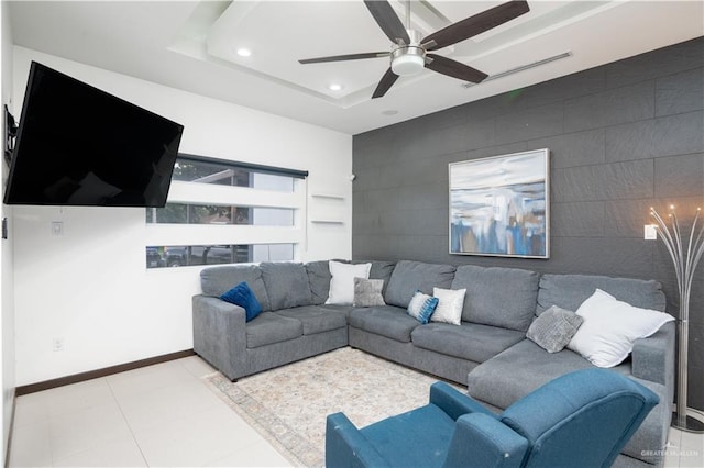 living room with an accent wall, recessed lighting, a ceiling fan, baseboards, and a raised ceiling