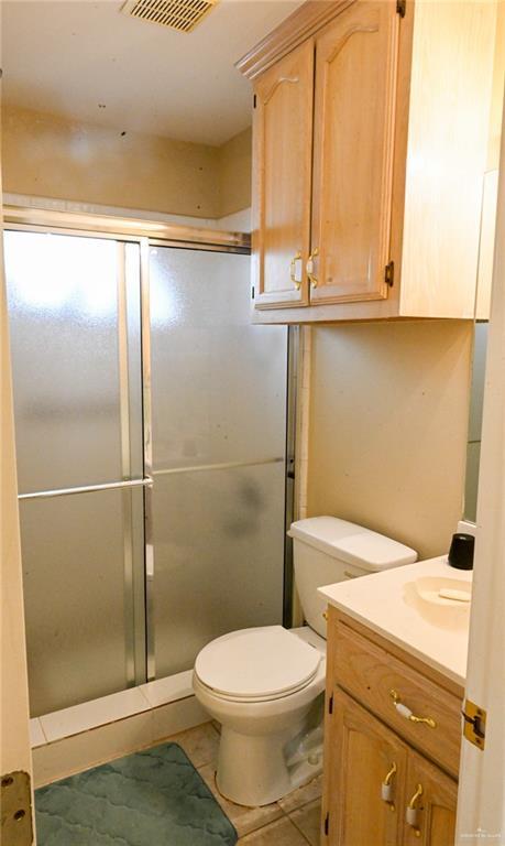 bathroom with tile patterned flooring, vanity, a shower with shower door, and toilet