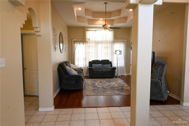 tiled living room with a raised ceiling and ceiling fan