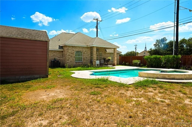 view of swimming pool featuring an in ground hot tub, a yard, cooling unit, and a storage shed