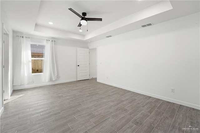 spare room with a tray ceiling, ceiling fan, and light wood-type flooring