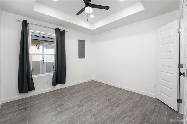 spare room featuring a tray ceiling, electric panel, ceiling fan, and hardwood / wood-style floors