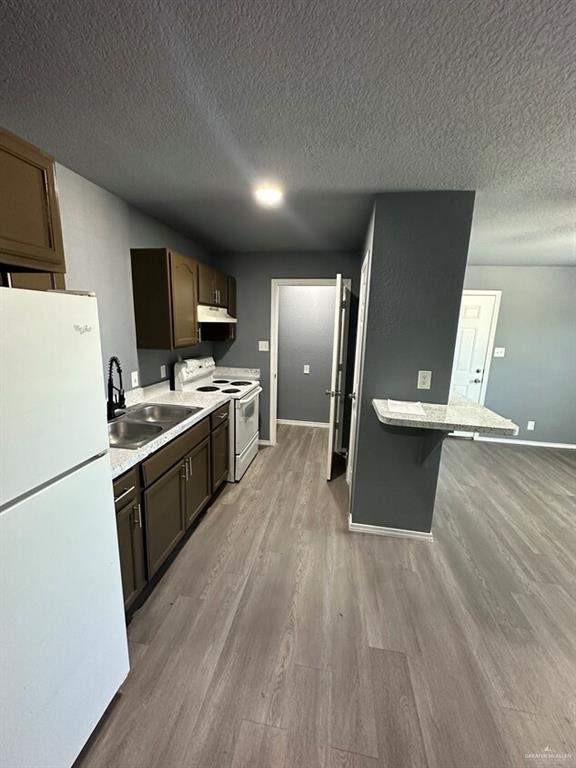 kitchen with white appliances, a breakfast bar, sink, hardwood / wood-style flooring, and dark brown cabinetry