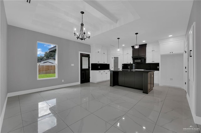 kitchen with a notable chandelier, a raised ceiling, an island with sink, and white cabinets