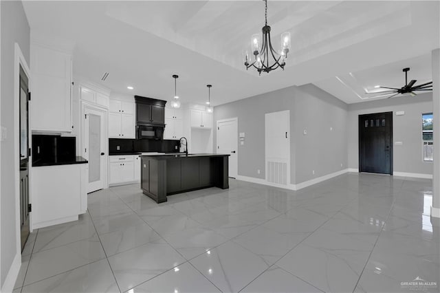 kitchen with pendant lighting, a tray ceiling, white cabinets, and a center island with sink