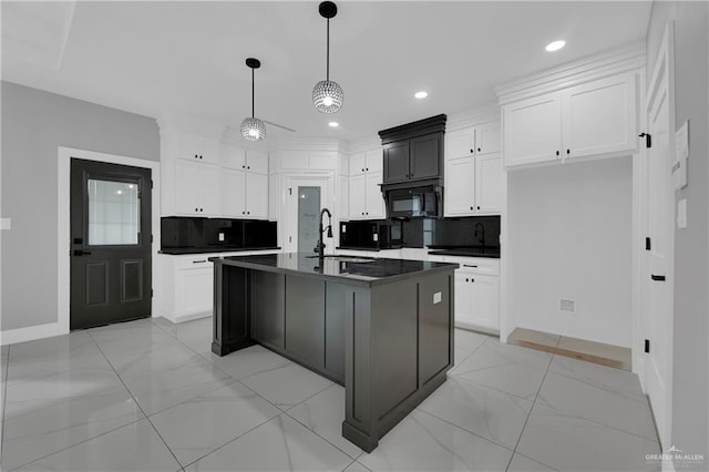 kitchen featuring decorative light fixtures, tasteful backsplash, white cabinetry, sink, and a center island with sink