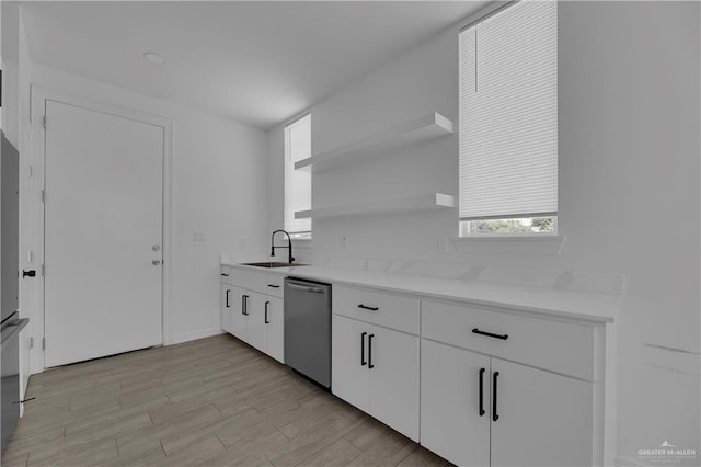 kitchen with white cabinets, sink, light hardwood / wood-style flooring, stainless steel dishwasher, and light stone counters