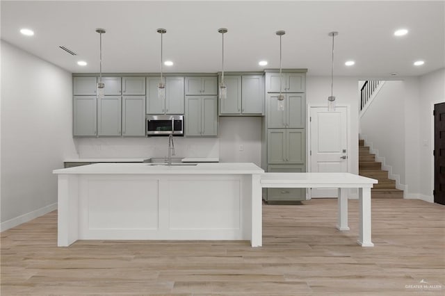 2615 E Solar Dr, Mission, TX 78574 - kitchen featuring stainless steel microwave, light wood-style floors, light countertops, recessed lighting, and an island with sink
