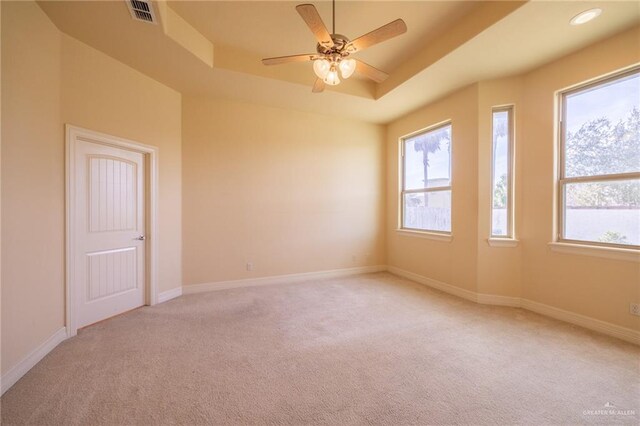 unfurnished room featuring a raised ceiling, a wealth of natural light, ceiling fan, and light colored carpet