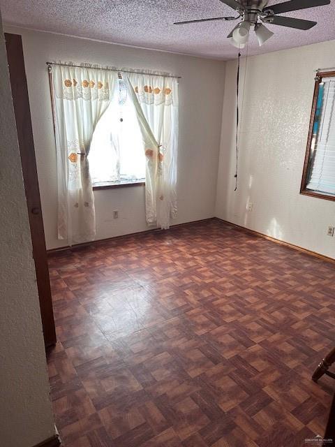 empty room featuring ceiling fan, dark parquet flooring, and a textured ceiling