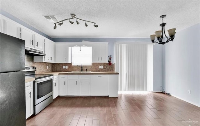 kitchen featuring sink, decorative light fixtures, stainless steel electric stove, black refrigerator, and white cabinets