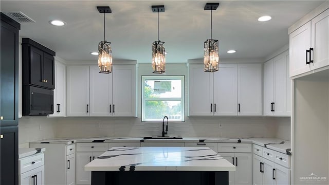 kitchen with visible vents, a center island, light stone countertops, black microwave, and a sink