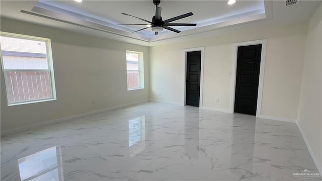 unfurnished bedroom with a ceiling fan, a tray ceiling, marble finish floor, and baseboards