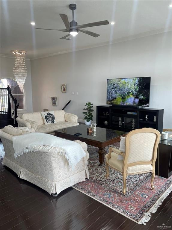 living room with ornamental molding, ceiling fan with notable chandelier, and dark wood-type flooring