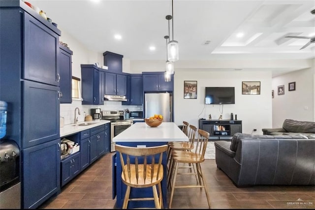 kitchen featuring wood finish floors, under cabinet range hood, appliances with stainless steel finishes, blue cabinets, and a sink