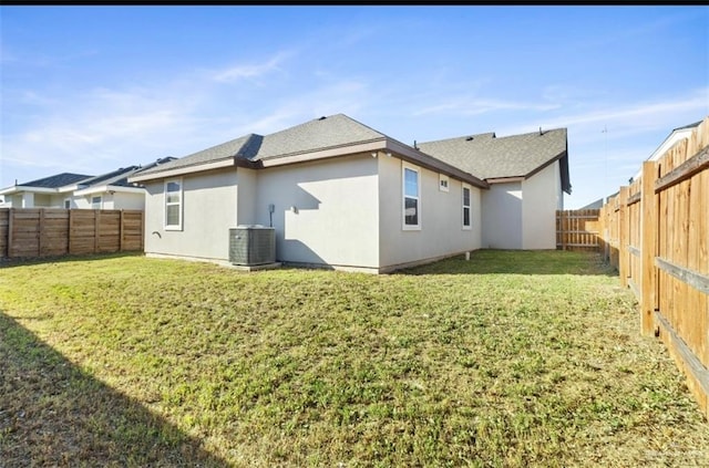 rear view of property featuring a yard, central AC, a fenced backyard, and stucco siding