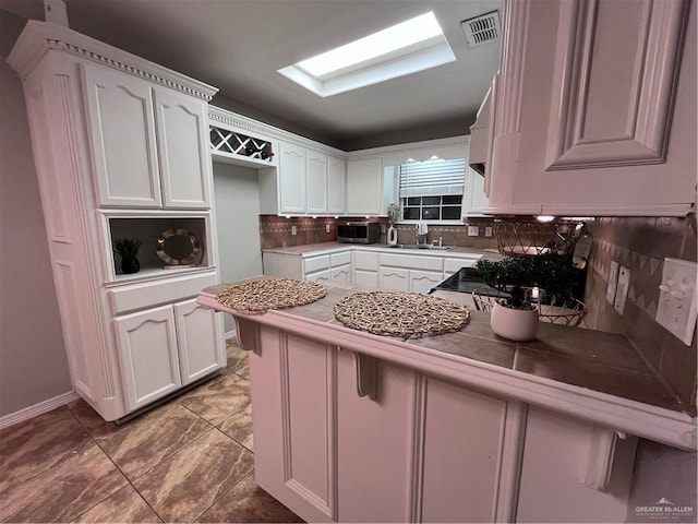 3404 Robin Ave, Pharr, TX 78577 - kitchen with stainless steel microwave, backsplash, a peninsula, white cabinetry, and a sink