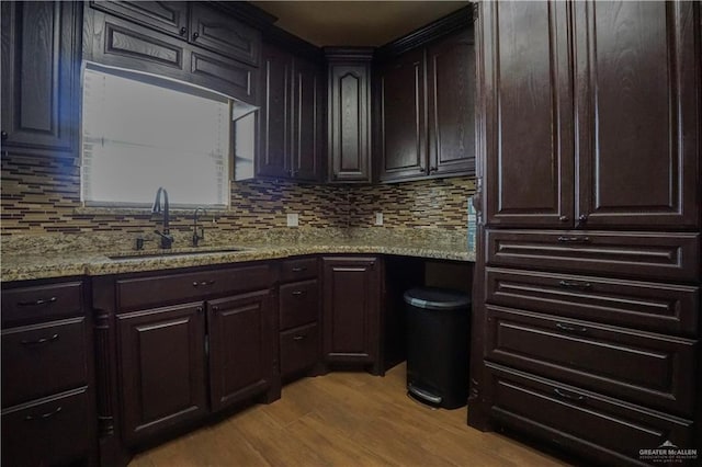 kitchen with dark brown cabinetry, sink, light hardwood / wood-style floors, and light stone countertops